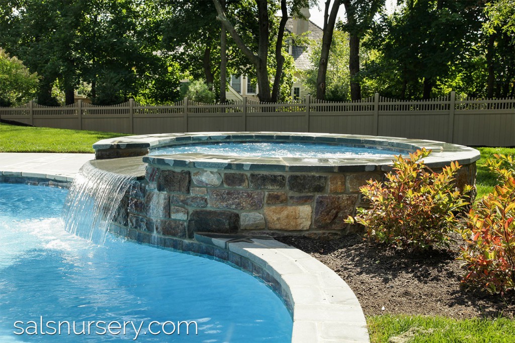 Round stone spa with waterfall into pool